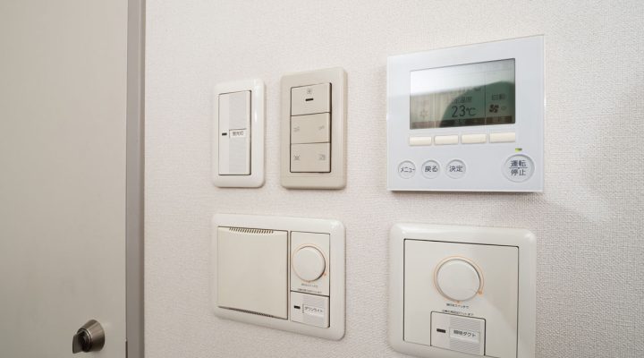 A wall-mounted control panel featuring dimmer switches, a thermostat, and other smart home controls.