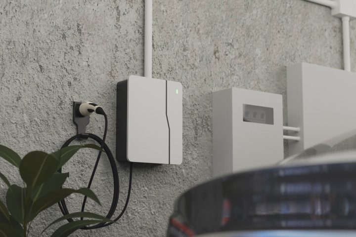An electric vehicle charging station mounted on an exterior wall, connected to a car for recharging.