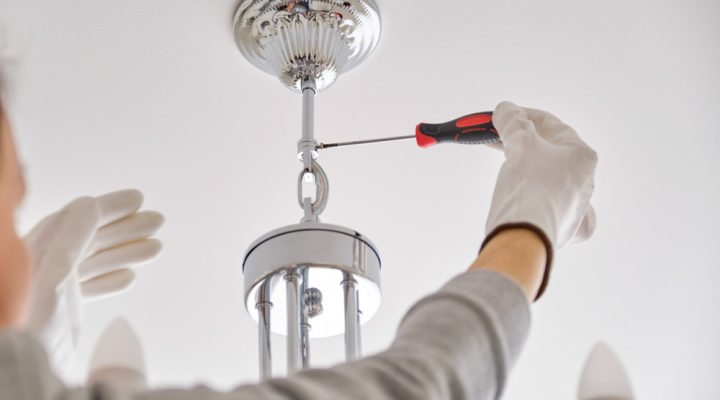 A person wearing gloves uses a screwdriver to install or adjust a ceiling light fixture.