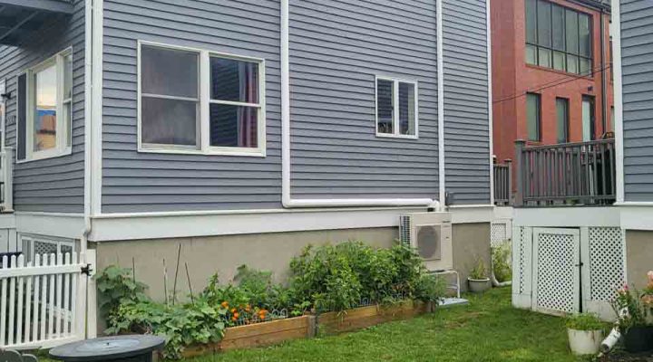 A two-story blue house with a well-maintained backyard featuring a garden, patio furniture, and a trampoline.