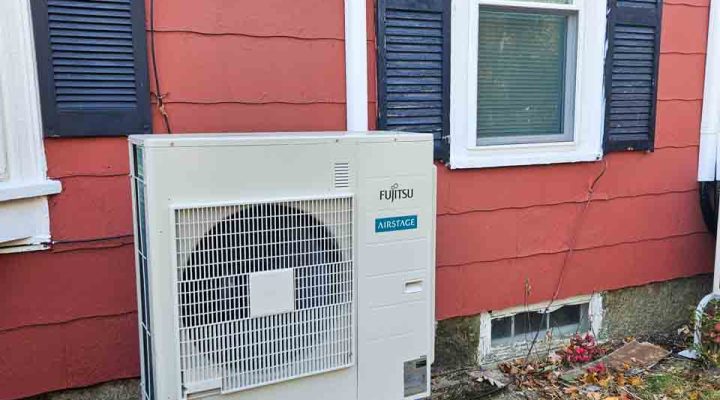 A Fujitsu air conditioning unit installed on the side of a red house, ensuring efficient climate control.