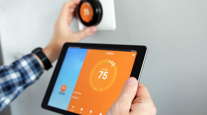 A person configures a smart thermostat using a tablet, demonstrating modern home automation technology.